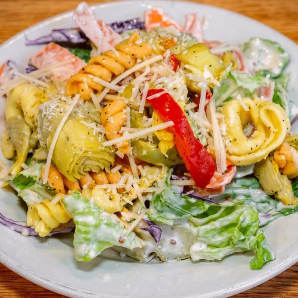 Creamy pasta salad with fusilli, vegetables, lettuce, artichoke hearts, red pepper, and shredded cheese on a plate.