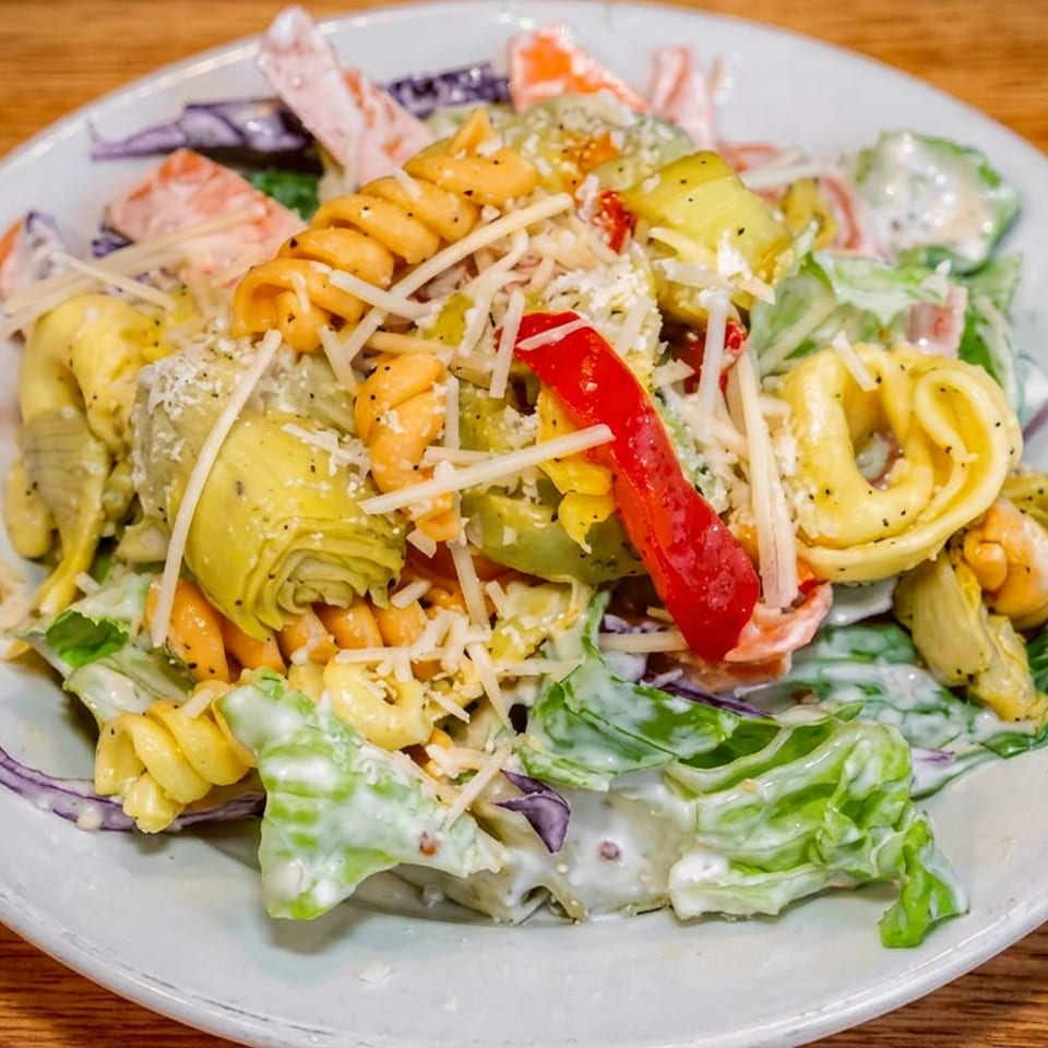 Creamy pasta salad with fusilli, vegetables, lettuce, artichoke hearts, red pepper, and shredded cheese on a plate.
