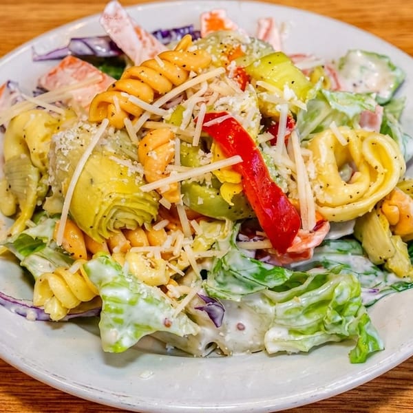 Creamy pasta salad with spiral noodles, artichokes, peppers, lettuce, chickpeas, and grated cheese on a plate.